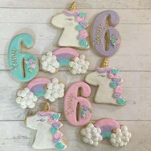 May include: A set of nine unicorn-themed sugar cookies decorated with pastel colors, including pink, blue, purple, and white. The cookies feature unicorns, rainbows, and the number six. The cookies are perfect for a unicorn-themed birthday party.