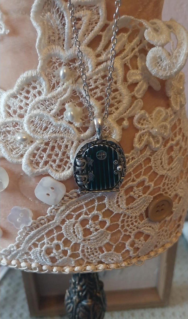 Pu&ograve; includere: Una collana con catena d'argento con un ciondolo a forma di porta verde. La porta &egrave; decorata con una cornice d'argento e una piccola manopola d'argento. Il ciondolo &egrave; attaccato a una catena d'argento.