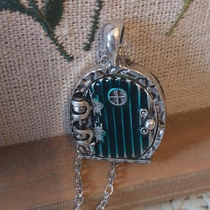 Pu&ograve; includere: Una collana d'argento con un ciondolo a forma di porta verde. La porta ha una piccola finestra e una maniglia d'argento. La catena &egrave; d'argento e ha una chiusura a moschettone.