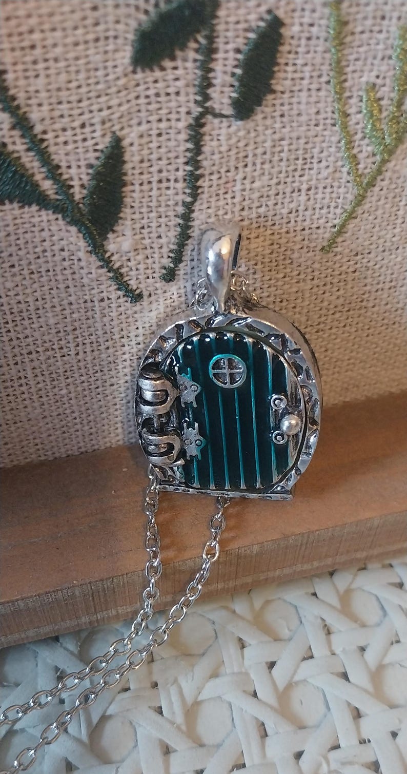 Pu&ograve; includere: Una collana d'argento con un ciondolo a forma di porta verde. La porta ha una piccola finestra e una maniglia d'argento. La catena &egrave; d'argento e ha una chiusura a moschettone.
