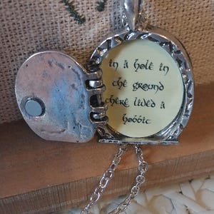Pu&ograve; includere: Una collana con un ciondolo d'argento con una citazione de Il Signore degli Anelli: "In un buco nel terreno viveva uno hobbit". Il ciondolo &egrave; aperto, rivelando un interno color crema con lettere nere.