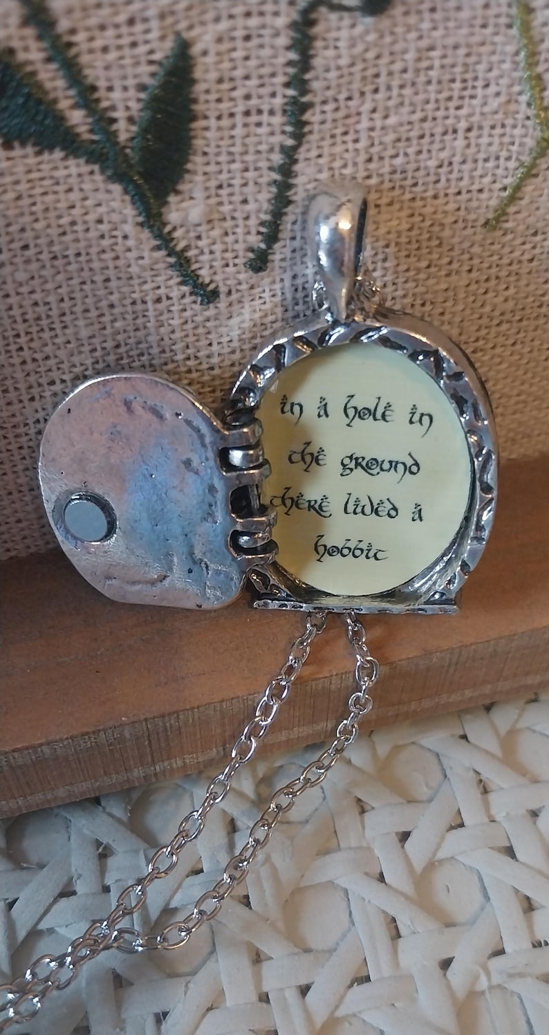 Pu&ograve; includere: Una collana con un ciondolo d'argento con una citazione de Il Signore degli Anelli: "In un buco nel terreno viveva uno hobbit". Il ciondolo &egrave; aperto, rivelando un interno color crema con lettere nere.