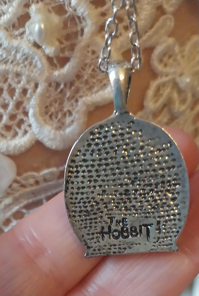 Pu&ograve; includere: Collana d'argento con un ciondolo rotondo che presenta un'immagine dettagliata di uno hobbit. Il ciondolo ha il testo "The Hobbit" inciso sul retro.