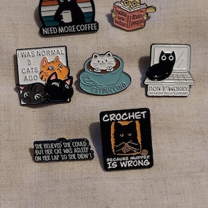 Puede incluir: Colección de pines de esmalte con diseños de gatos. Los pines incluyen un gato negro con una taza de café, un gato leyendo un libro, un gato en una taza de capuchino y un gato en un portátil. Otros pines tienen el texto: "I was normal 3 cats ago."