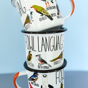 May include: Three white enamel mugs stacked, each featuring bird illustrations and the words "FOWL LANGUAGE." The top mug has an orange handle. Birds include a Southern Screamer and a Red-Billed Woodpecker. The middle mug features a Tufted Titmouse.