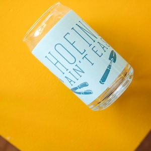 May include: A clear glass with a white label that says "HOFLIN' AINT' EASY". The label has a blue design of tools on it.