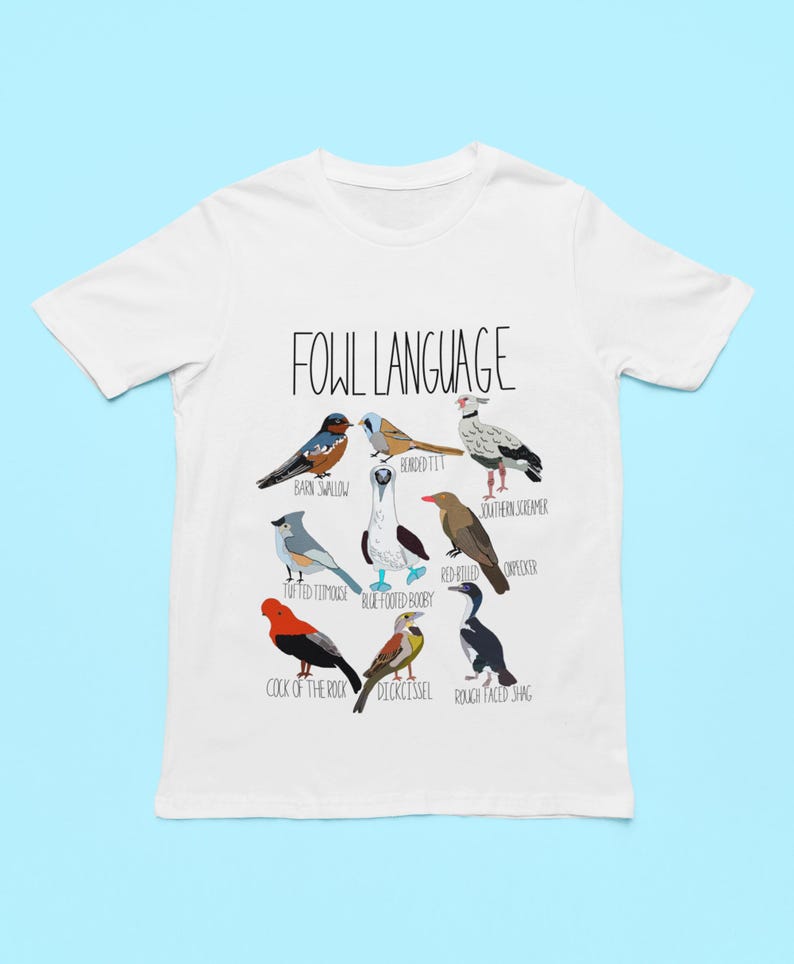 White unisex t-shirt with 'Fowl Language' bird design featuring tufted titmouse, blue-footed booby, and more. Flat lay on light blue background, perfect for bird lovers and humor fans.