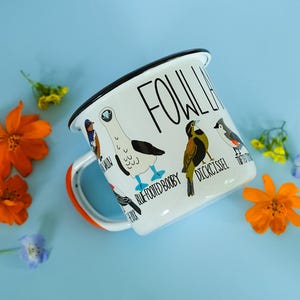May include: White enamel mug with a black rim and handle, featuring bird illustrations and the text "FOWL LIFE." The mug has an orange accent on the handle and is decorated with various bird species, including a Blue-Footed Booby.