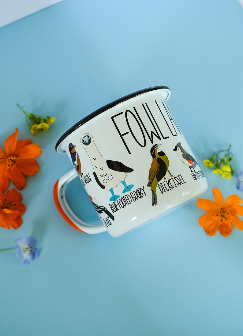 May include: White enamel mug with a black rim and handle, featuring bird illustrations and the text "FOWL LIFE." The mug has an orange accent on the handle and is decorated with various bird species, including a Blue-Footed Booby.