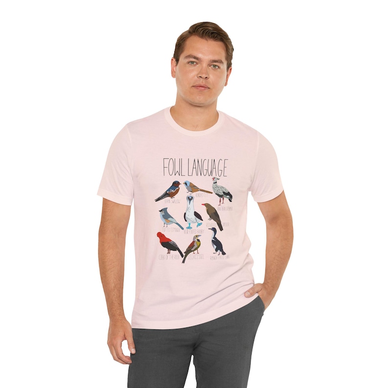 Soft pink unisex t-shirt with 'Fowl Language' bird design featuring tufted titmouse, blue-footed booby, and more on male model.