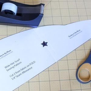 May include: A white sewing pattern for a wide hair scarf with the text "Sewing to the Moon" and "www.sewingtothemoon.com". The pattern includes instructions to cut two pieces of fabric and to use a 1/4 inch seam allowance.
