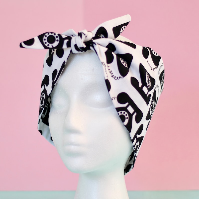 May include: A white and black patterned headband with a design of old-fashioned rotary phones. The headband is tied in a knot on top of the head.