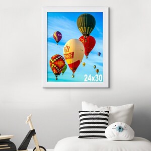以下が含まれることがあります： 青い空を背景に、カラフルな熱気球が描かれた白い額縁。額縁のサイズは24インチ×30インチです。