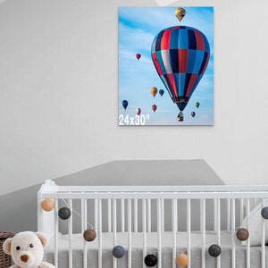 May include: A colorful hot air balloon with red, blue, and white stripes against a blue sky with white clouds. The balloon is surrounded by other smaller hot air balloons. The image is labeled "24x30".
