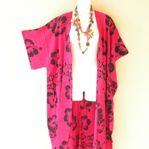 May include: A pink and black floral print kimono with a fringe hem. The kimono has short sleeves and is open in the front. A colorful beaded necklace is worn over the kimono.