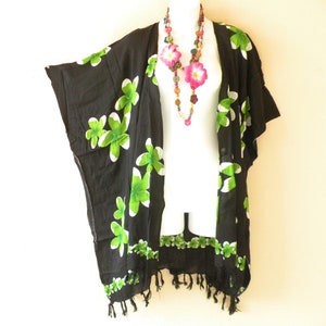 May include: Black kimono with green and white floral print and fringe trim. The kimono is worn on a white mannequin with a multi-colored beaded necklace and pink flower accents.