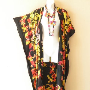 May include: Black kimono with a floral print in shades of yellow, orange, and red. The kimono has a fringed hem and is open in the front. A colorful beaded necklace is worn over the kimono.