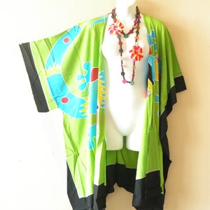 May include: Green kimono with a colorful abstract design and black trim. The kimono is worn on a white mannequin with a multi-colored beaded necklace.