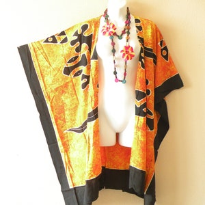 May include: A yellow and black patterned kimono with a black trim. The kimono is worn on a white mannequin and features a multi-colored beaded necklace with flower accents.