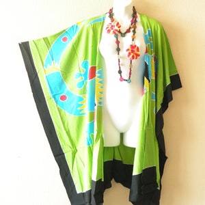 May include: A green kimono with black trim and colorful abstract designs. The kimono is worn on a white mannequin with a multi-colored wooden bead necklace.