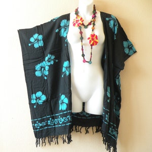 May include: Black kimono-style cover-up with turquoise hibiscus flower print and fringe trim. A colorful necklace with flower and bead accents is draped over a mannequin. The cover-up is lightweight and suitable for beachwear or casual wear.