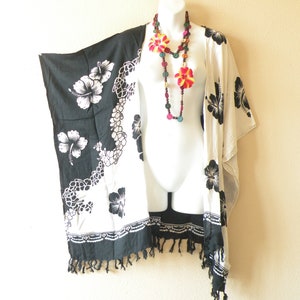 May include: Black and white floral print kimono with a colorful wooden bead necklace. The kimono has a fringed hem and is made of a lightweight fabric.