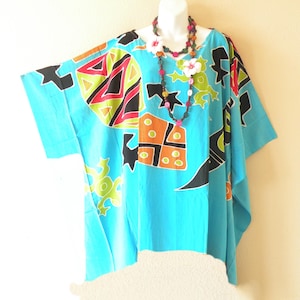 May include: A turquoise caftan with a colorful geometric pattern featuring red, black, green, and orange shapes. The caftan has short sleeves and a loose fit. A beaded necklace with flower accents is draped around the neckline.