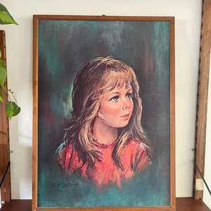 Puede incluir: Una pintura enmarcada de una niña joven con el pelo largo y rubio que lleva un jersey rojo. El fondo es de color azul verdoso oscuro. La pintura está firmada "E.P.Yri" en la esquina inferior izquierda.