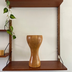 Könnte beinhalten: Eine Holzvase mit einer einzigartigen Sanduhrform, die auf einem Holzregal steht.