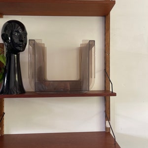 May include: A set of brown plastic magazine holders on a wooden shelf unit. The shelf unit has a black head sculpture and a black and white planter on the top shelf.