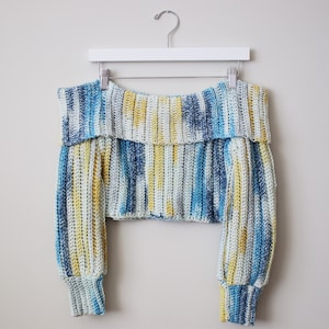 Könnte beinhalten: Ein blauer und gelber gestreifter, gehäkelter Pullover mit Off-Shoulder-Ausschnitt und langen Ärmeln.