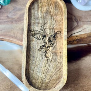 May include: A wooden oval tray with a dark wood finish and a laser-etched design of an owl in flight. The owl is surrounded by a swirling design.