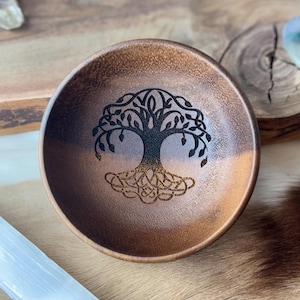 Könnte beinhalten: Eine Holzschale mit einem eingravierten Lebensbaum-Design. Die Schale ist braun und hat eine natürliche Holzoptik.