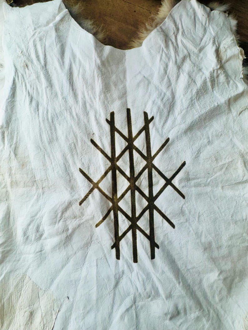 Puede incluir: Una prenda de cuero blanco con un dise&ntilde;o geom&eacute;trico en pintura dorada. El dise&ntilde;o es una serie de l&iacute;neas que se cruzan formando una cuadr&iacute;cula.