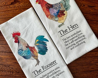 May include: Two kitchen towels with illustrations of a rooster and a hen. The rooster towel has the text "The Rooster" and a description of the rooster's symbolism. The hen towel has the text "The Hen" and a description of the hen's symbolism.