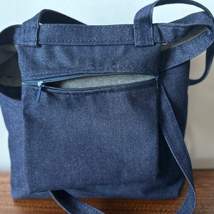 May include: A dark blue denim tote bag with a zippered pocket on the front. The bag has two long straps.