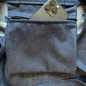 May include: A dark blue denim tote bag with a zippered pocket. A black smartphone with a camera lens is in the pocket.