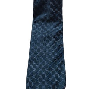 May include: A dark navy blue necktie featuring a repeating tonal pattern of the interlocking GG logo across the entire surface. The fabric has a subtle sheen, and the tie is shaped with a pointed end, displaying a consistent monogram design.