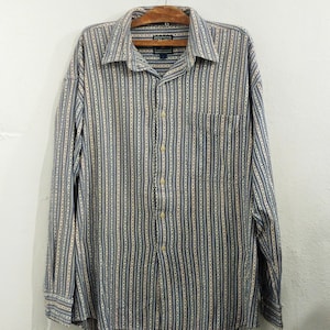 May include: A long-sleeved button-down shirt with a vertical striped pattern in blue, beige, and white. The shirt has a collared neckline, a chest pocket, and buttoned cuffs. The shirt is hanging on a wooden hanger.
