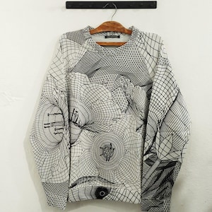 Könnte beinhalten: Ein langärmliges Sweatshirt mit Rundhalsausschnitt und einem komplexen schwarz-weißen geometrischen Design. Das Muster zeigt sich kreuzende Linien und kreisförmige Formen, die einen 3D-Effekt erzeugen. Das Sweatshirt hängt an einem Holzbügel.
