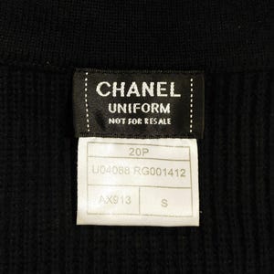 May include: Close-up of a black garment with two attached tags. The top tag reads "CHANEL UNIFORM NOT FOR RESALE" in white text. The bottom tag has the numbers "20P" and "U04088 RG001412" printed on it. The size is "S".