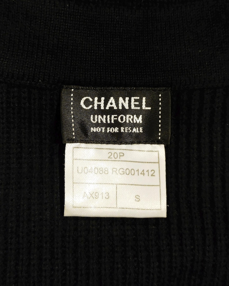 May include: Close-up of a black garment with two attached tags. The top tag reads "CHANEL UNIFORM NOT FOR RESALE" in white text. The bottom tag has the numbers "20P" and "U04088 RG001412" printed on it. The size is "S".