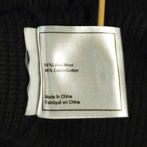 May include: Close-up of a white clothing tag with black text. The tag reads "54% Laine-Wool, 46% Coton-Cotton" and "Made In China, Fabriqu&eacute; en Chine". The tag is attached to a black fabric.