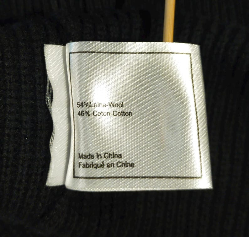 May include: Close-up of a white clothing tag with black text. The tag reads "54% Laine-Wool, 46% Coton-Cotton" and "Made In China, Fabriqu&eacute; en Chine". The tag is attached to a black fabric.