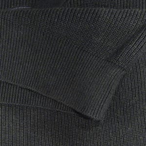 May include: Close-up of a section of a dark gray knit garment, possibly a sweater or jacket. The fabric has a ribbed texture, with visible vertical lines. The sleeve cuff is visible, showing the folded edge and the knit pattern.