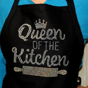 May include: Black apron with the text "Queen of the Kitchen" in silver rhinestones. A silver rhinestone crown is above the text and a rolling pin is below the text.