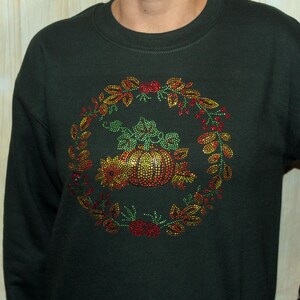May include: A dark green sweatshirt with a sparkly pumpkin and autumn leaves design. The design is made of rhinestones in shades of green, red, and gold.