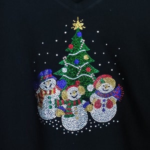 May include: A black Christmas jumper featuring a green, red and blue Christmas tree and three snowmen made of rhinestones.