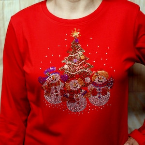 May include: Red long-sleeved shirt featuring a Christmas tree and three snowmen design made of rhinestones.