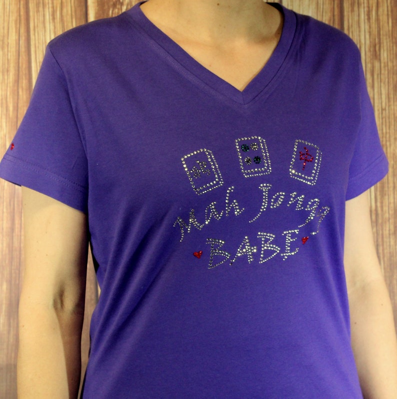 May include: Purple short-sleeved t-shirt with a rhinestone design that says "Mah Jongg Babe" with three mah jongg tiles.